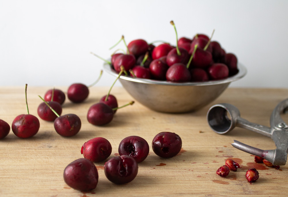 Lots of cherries in a metal bowl and a few pitted on a cutting board
