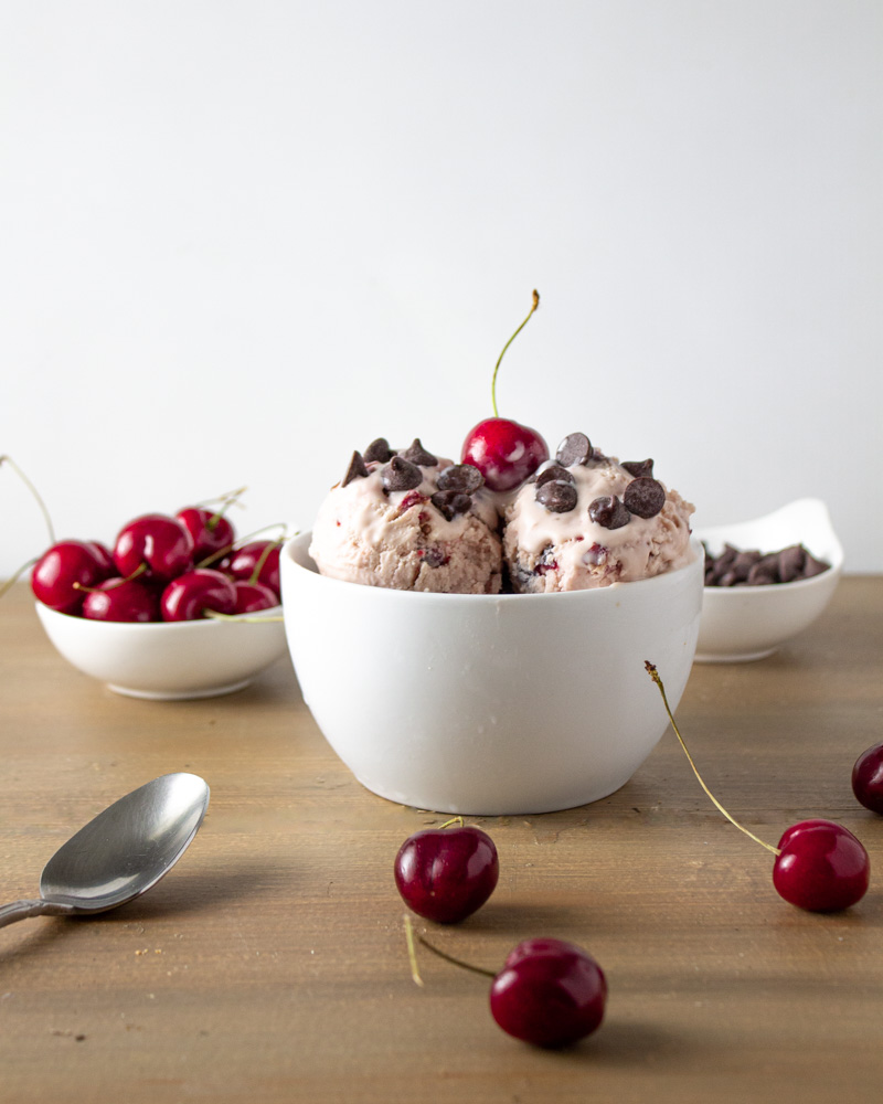 White bowl of ice cream with fresh cherries and chocolate chips