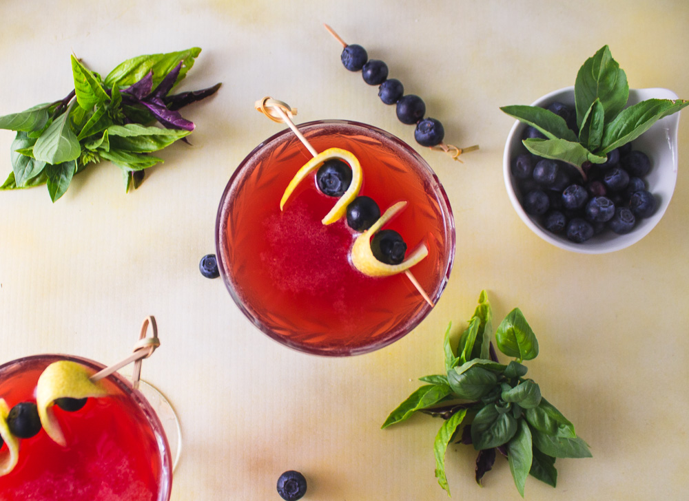 overhead shot of two blueberry basil shrub cocktails with basil and blueberries