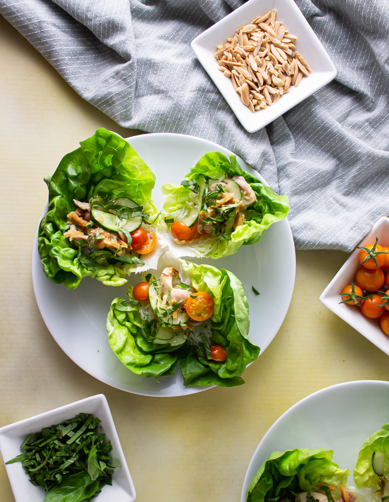 Over head image plates of chicken lettuce wraps with bowls of tomatoes almonds and basil
