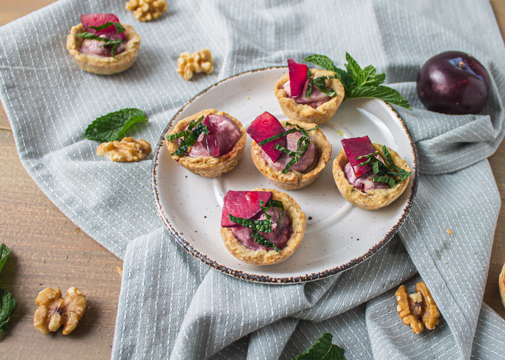 Angled shot of 1 plate of tarts on grey cloth with plum and walnuts