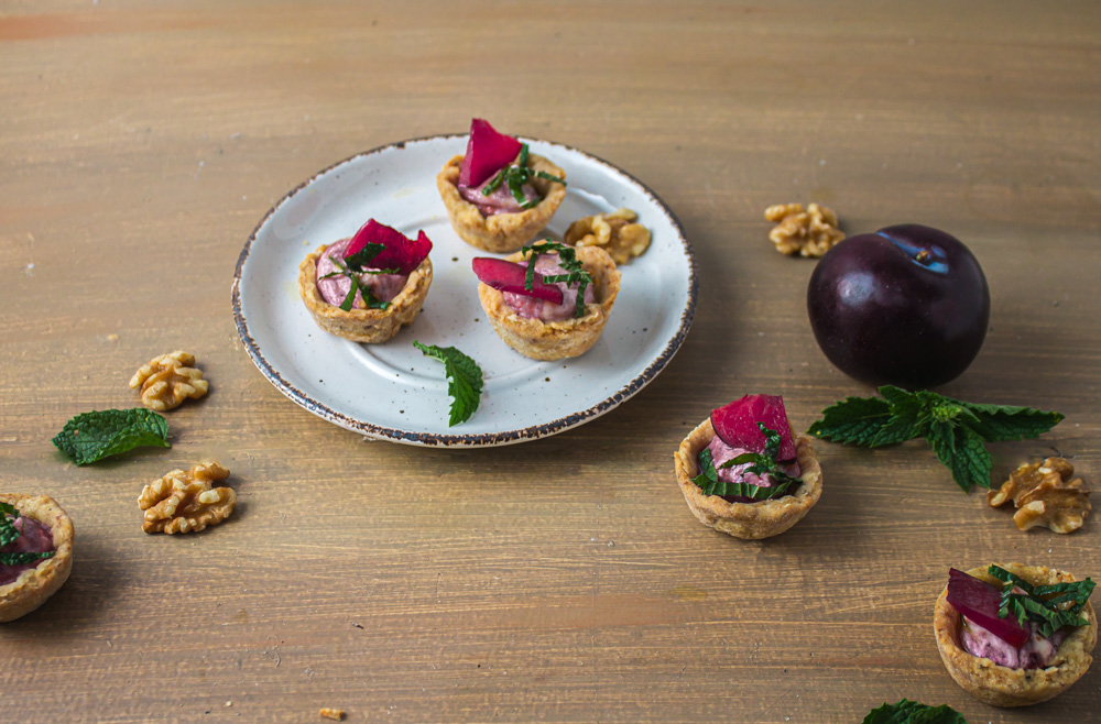 Angle shot of 1 plate of tarts on wood with plum and walnuts