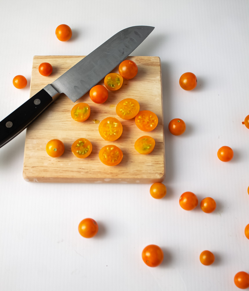 Sungold tomatoes partially cut on white background with knife