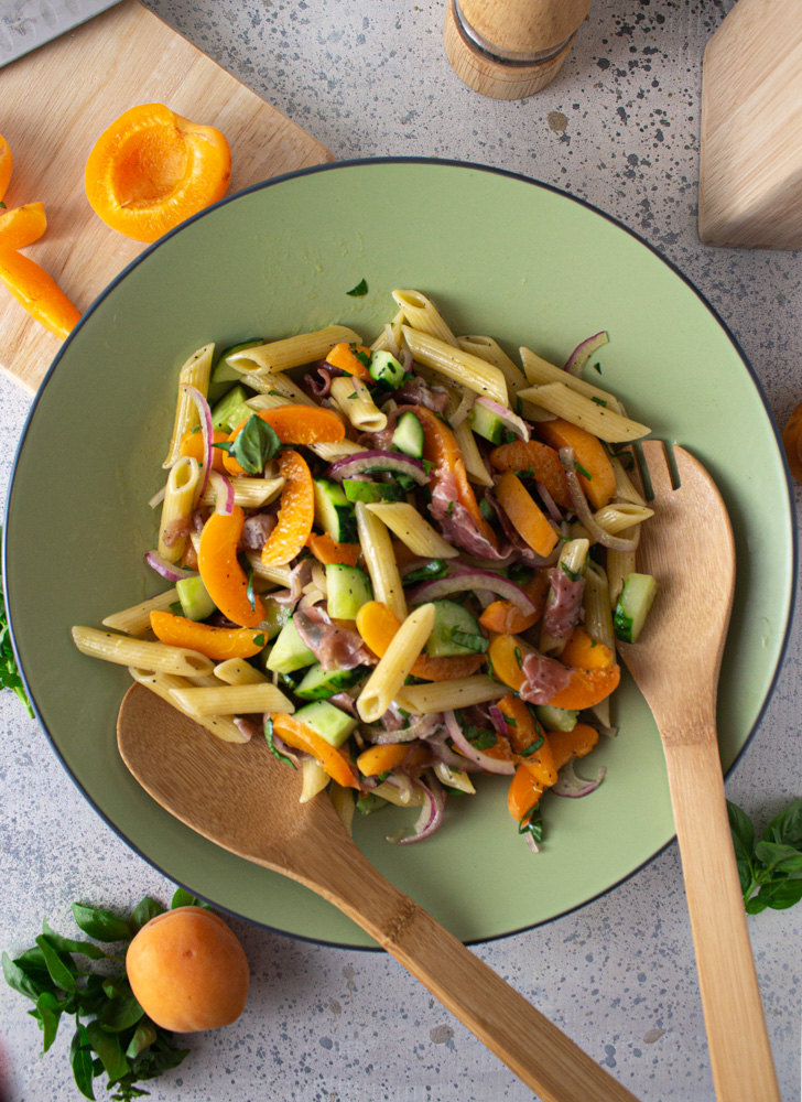 Top view of pasta salad in a green bowl with apricots