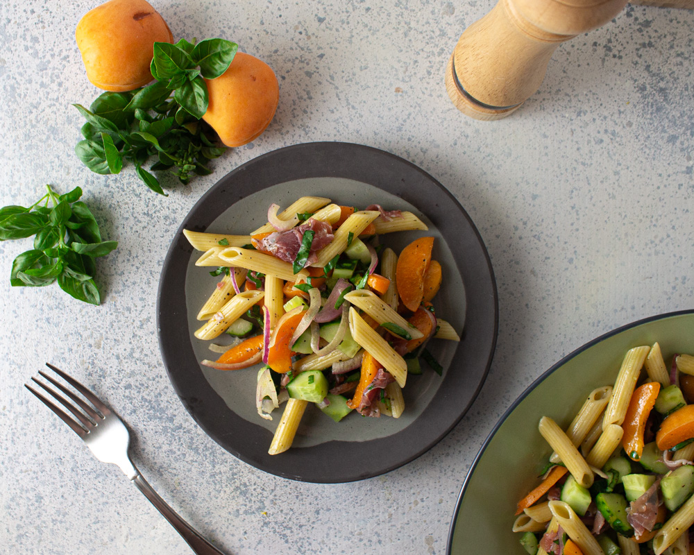 Top view of salad on a grey plate with green bowl to side and apricots