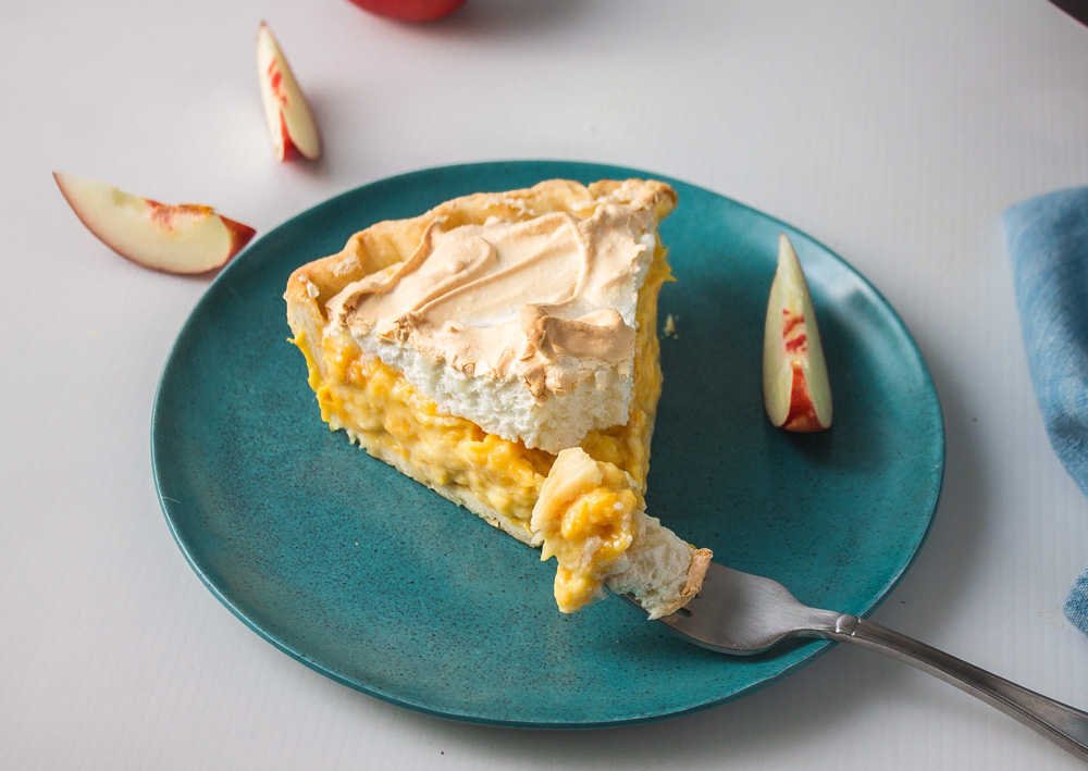 Slice of stone fruit meringue pie with fork ready to take a bite