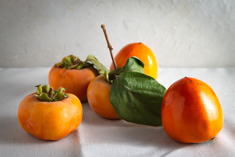 Fuyu and hachiya persimmons on a white background