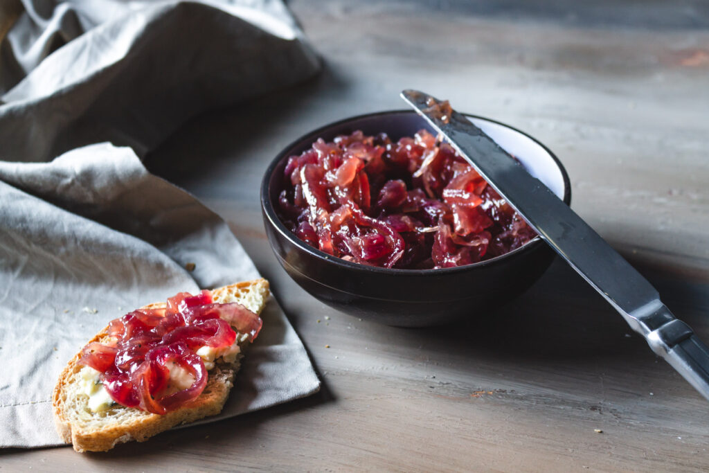 Bowl of onion wine jam with a piece of bread and cheese and a knife