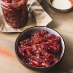 Small bowl and jar of onion jam on a wood table