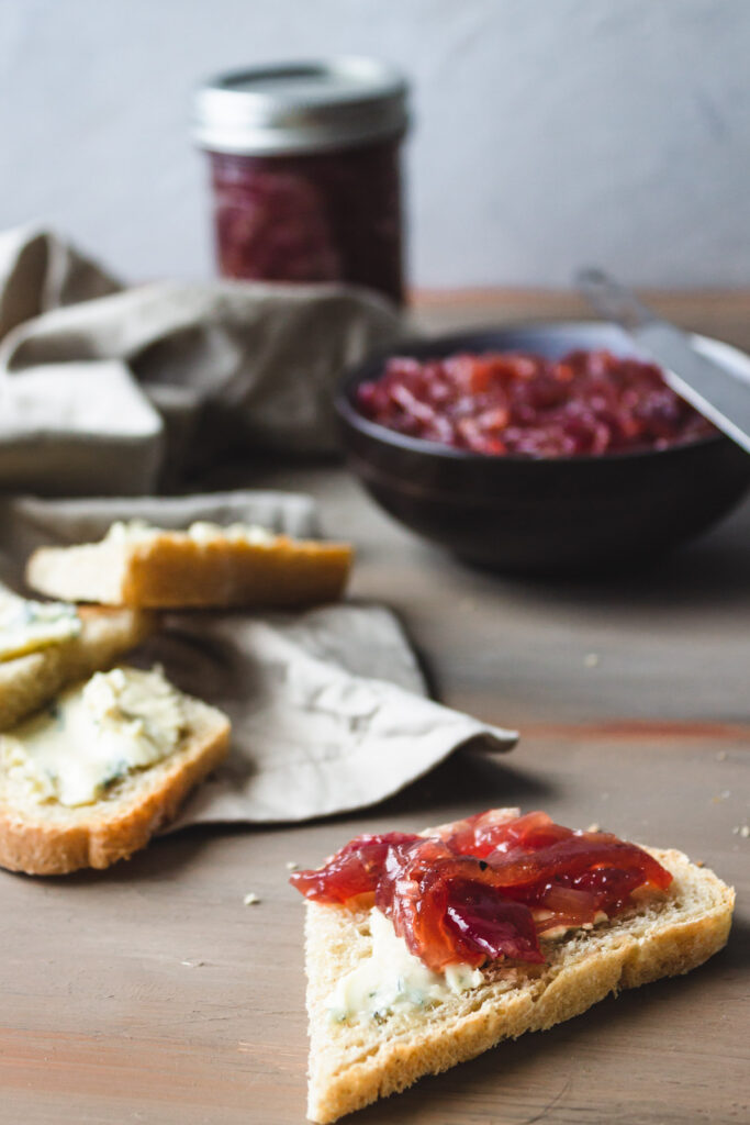 Tablescape of onion jam in jar, in a bowl, and on a piece of bread with several other pieces of bread