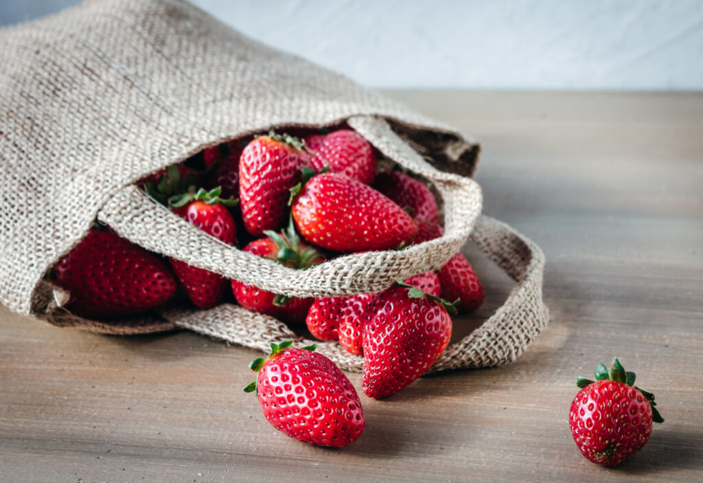 Hemp bag with fresh strawberries spilling out on a wood table