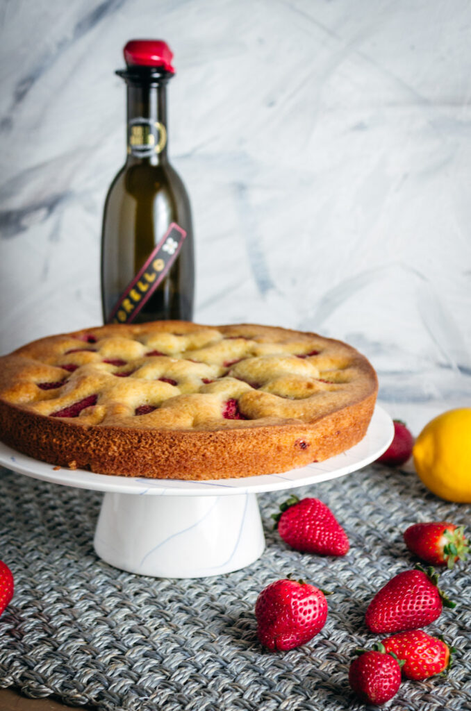 Whole strawberry olive oil cake on a cake stand with a bottle of olive oil