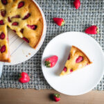 Strawberry Olive oil cake on a cake stand with a slice on a white plate