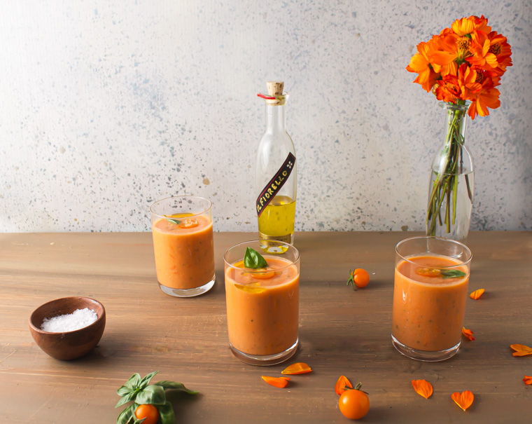 Three glasses of corn tomato gazpacho with flowers on table