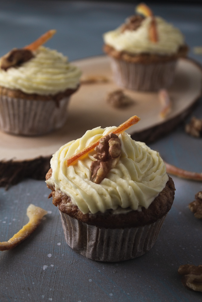 Angled view of 3 carrot cupcakes on wood plank