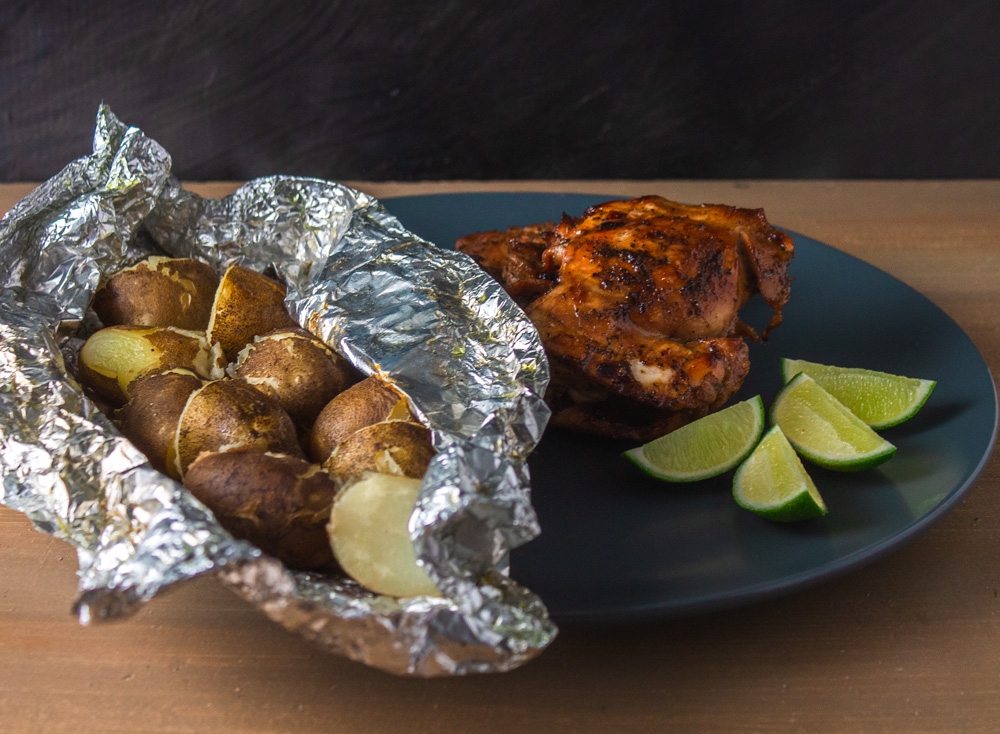 Potatoes in foil on grey plate with chicken and lime wedges