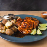 Side view of cooked marinated chicken and potatoes on grey plate with lime wedges