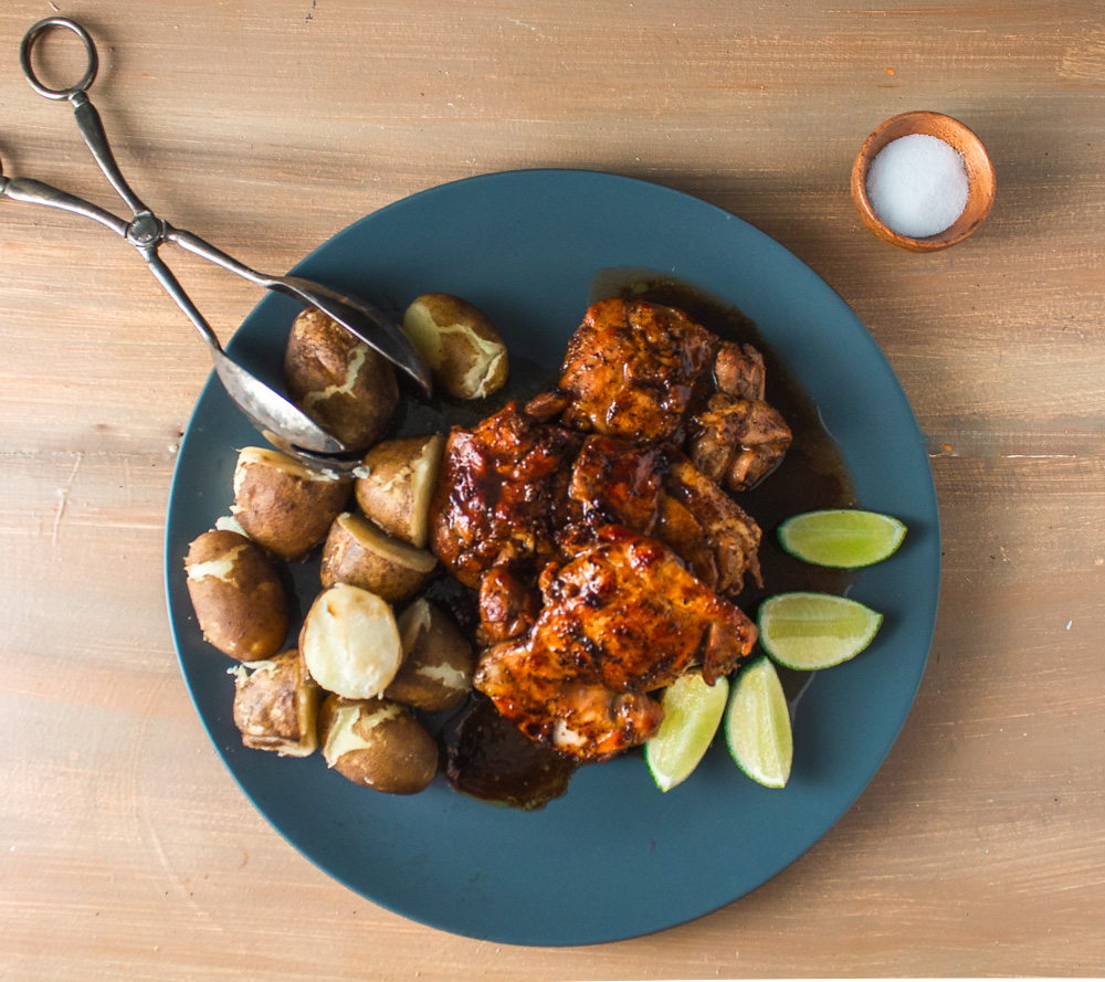 Top view of cooked marinated chicken and potatoes on grey plate with lime wedges
