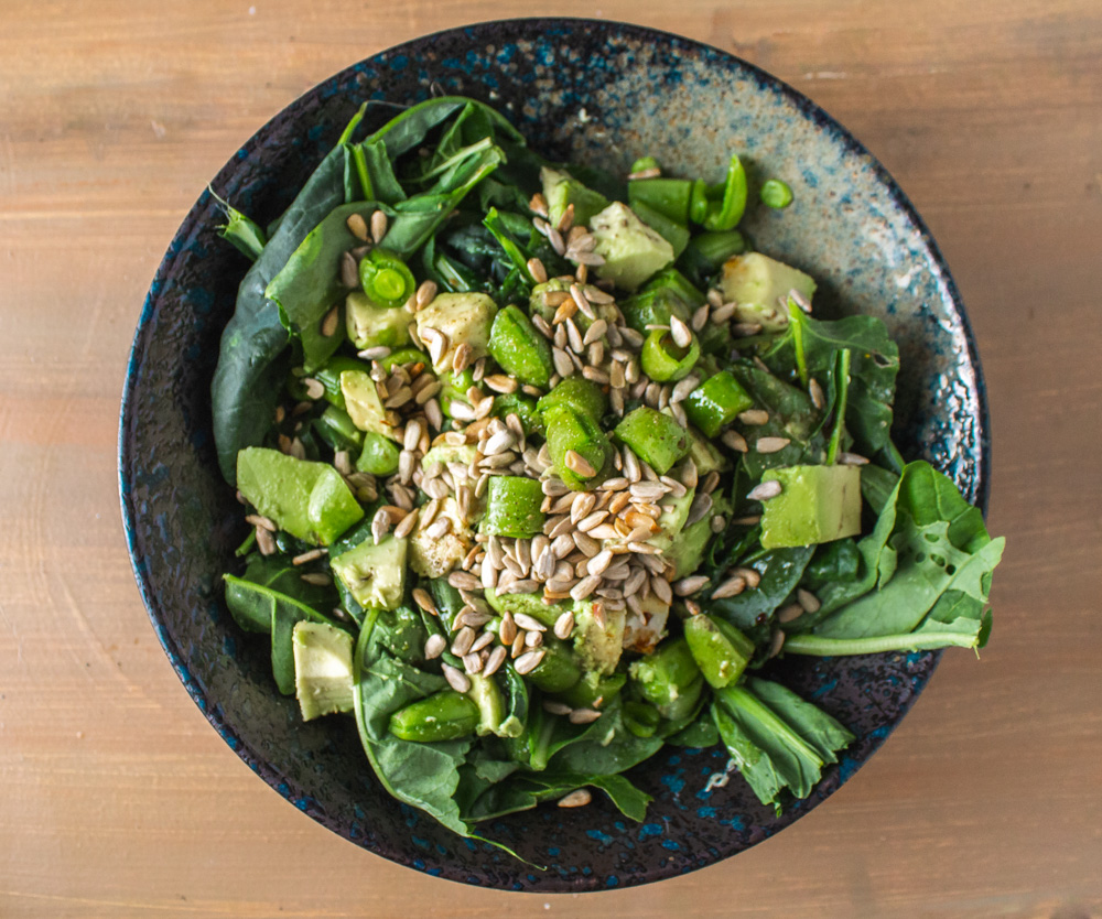 Salad of baby greens, snap peas, and avocado in a dark bowl