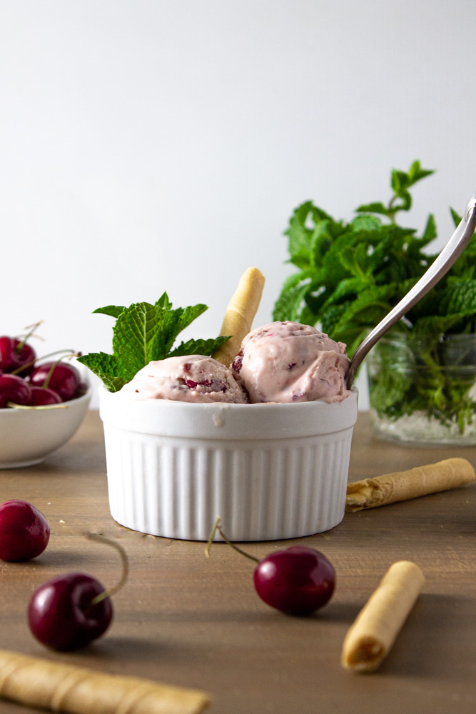 Side view of ice cream in a ramekin with cookies, mint and cherries