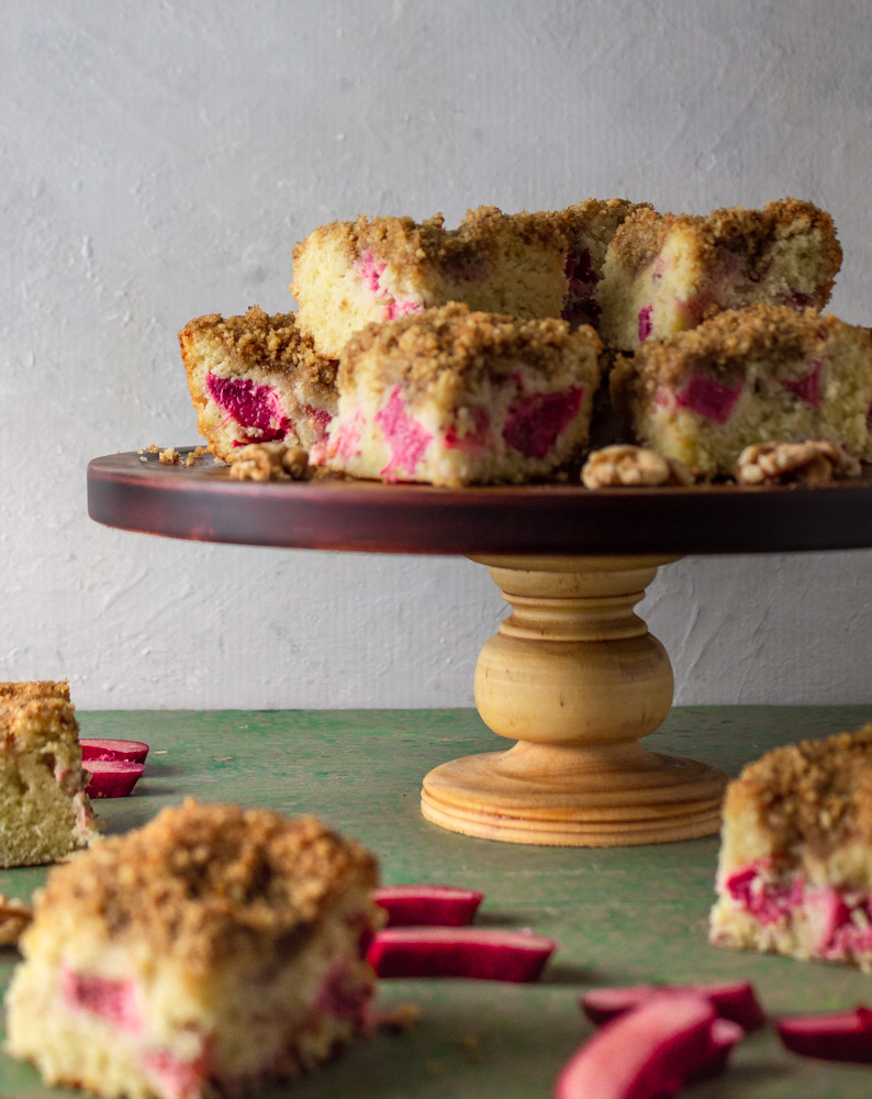 Side view of rhubarb cream cake on cake stand and green background