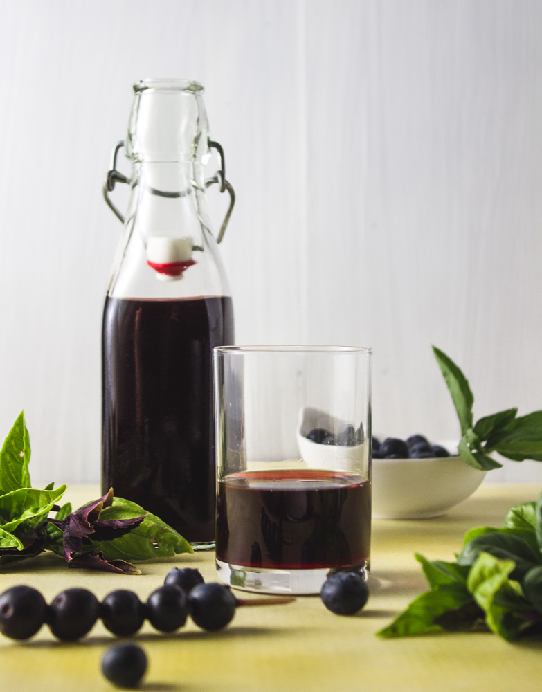 Bottle and glass of shrub with basil and blueberries