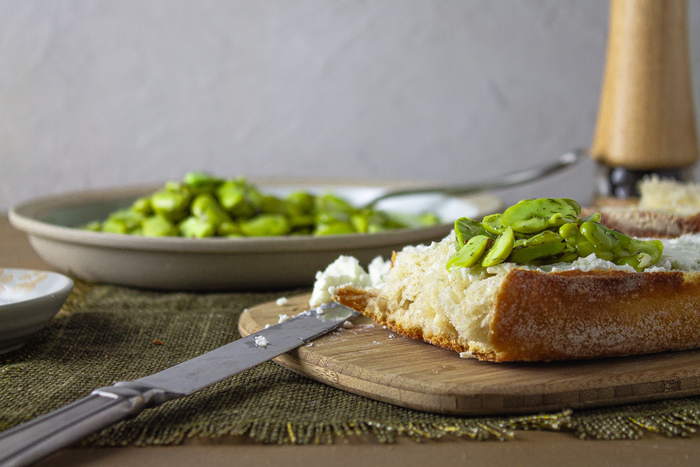 Side view of marinated fava beans on bread with goat cheese