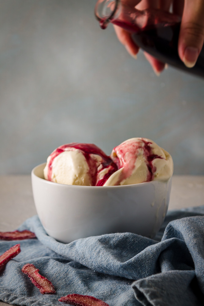 Pouring wine rhubarb syrup on ice cream in white bowl