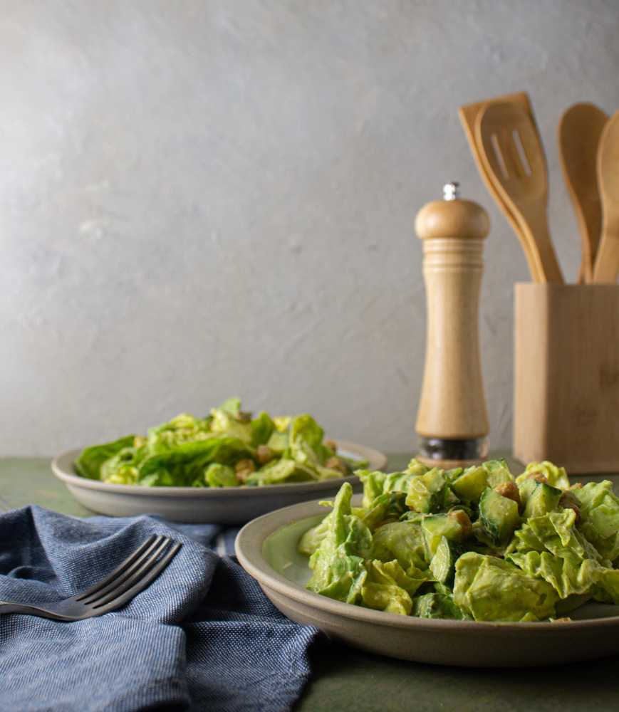 Side view of two salads with wooden utensils in background