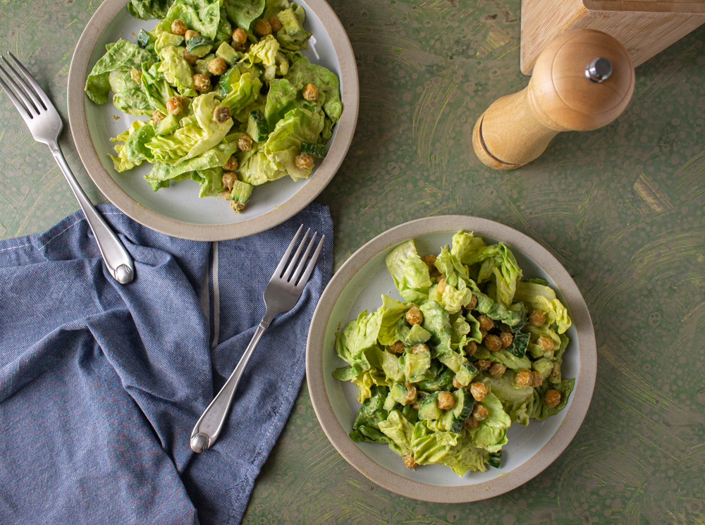 Top view of two salads on white plates with blue towel and forks