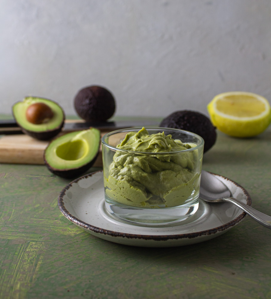 Glass bowl of dressing with avocados and lemons on cutting board