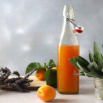 apricot lavender sage shrub in a bottle with lavender apricots and sage on blue background