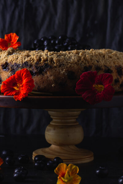 Side view of blueberry buckle on cake stand with nasturiums