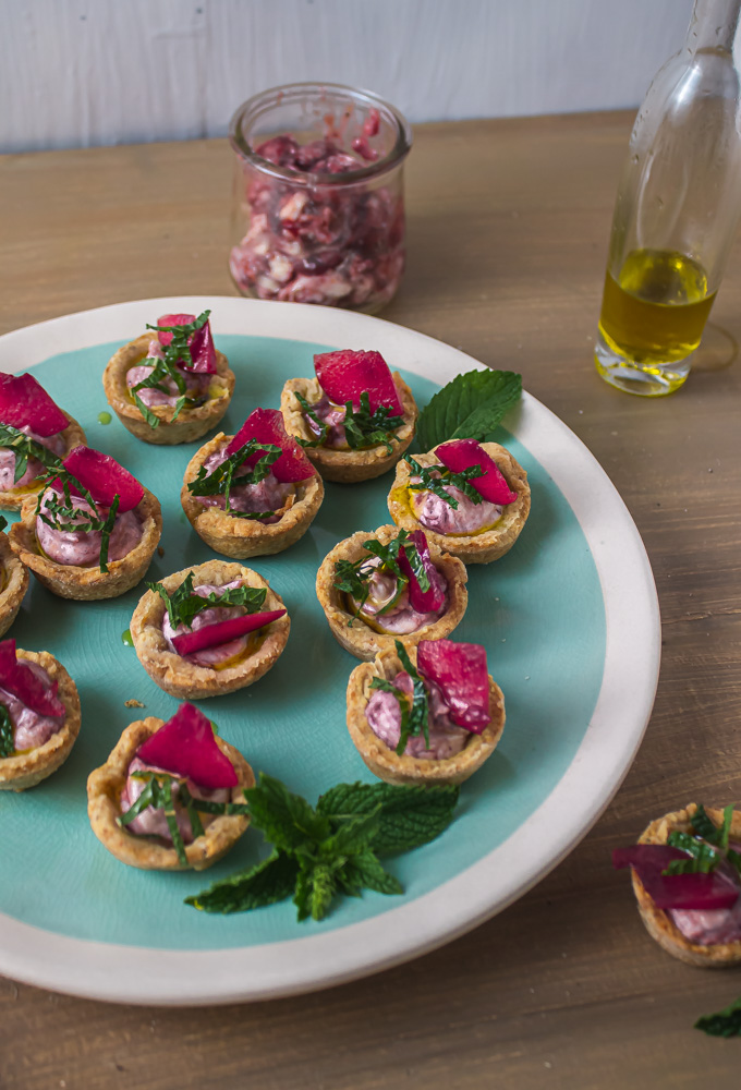 Angled shot of goat cheese plum tarts on green and white plate on wood