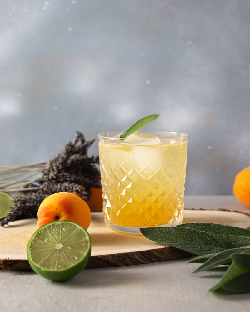 Apricot shrub spritz with fruit and lavender against a blue background