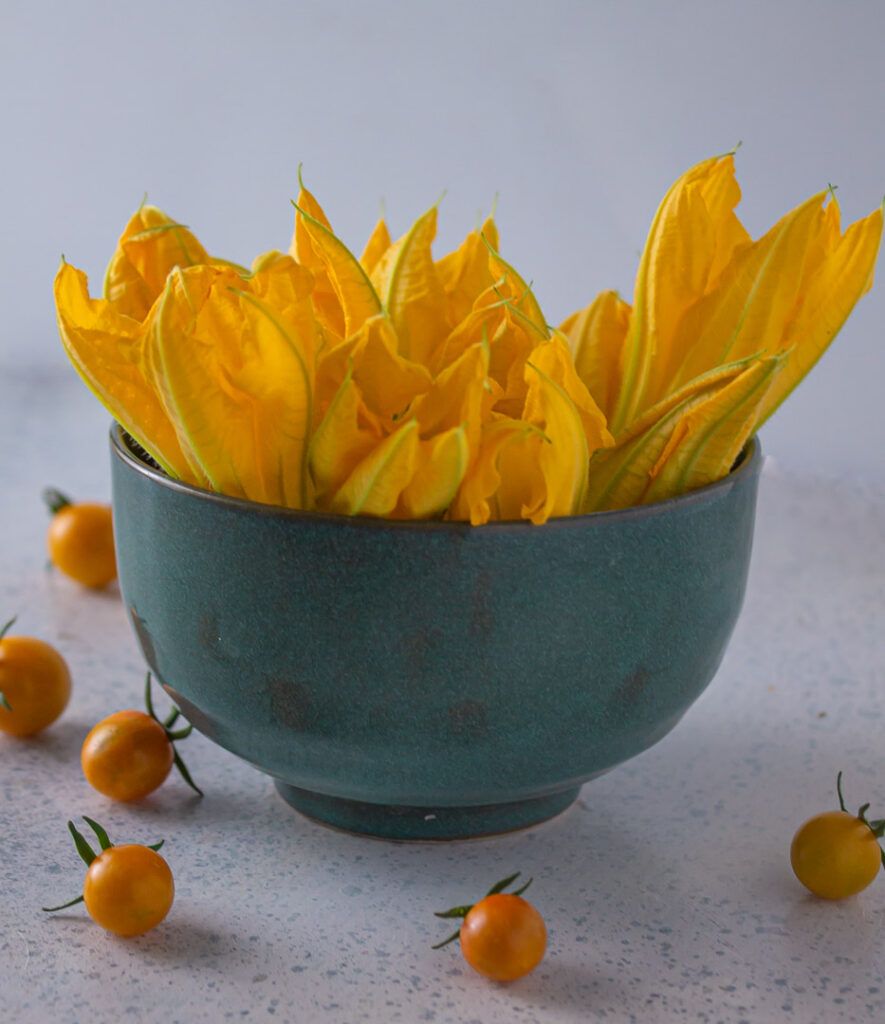 Blue bowl of squash blossoms with sun gold tomatoes scattered