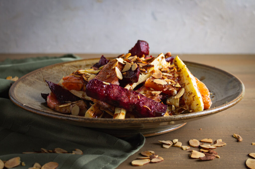 Roasted beets and parsnips with caracar oranges in a brown bowl on wood