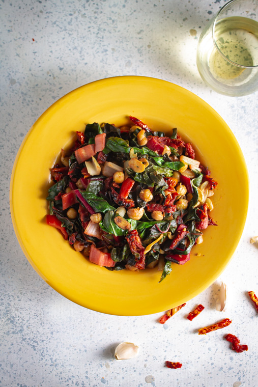 Overhead shot of sauteed chard and chickpeas in a hyellow bowl with a glass of white wine