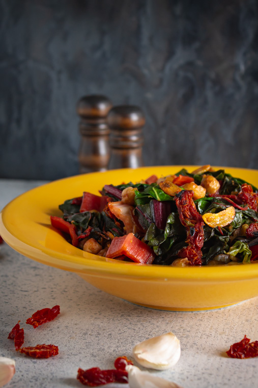 Side view of sauteed chard and chickpeas in a yellow bowl on a white speckled table