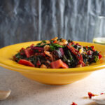 Yellow bowl with sauteed chard and chickpeas with glass of wine and pepper shaker