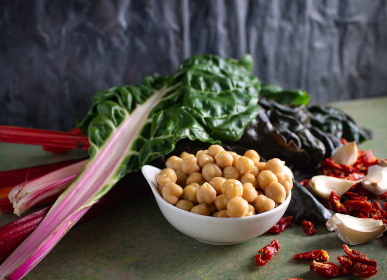 Ingredients: chard, chick peas, sun-dried tomato, and garlic on green background