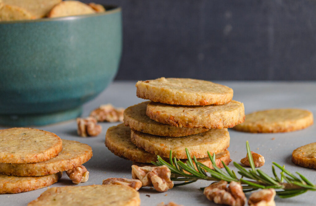 A stack of gorgonzola walnut cookies with rosemary and walnuts and a blue bowl in the background.