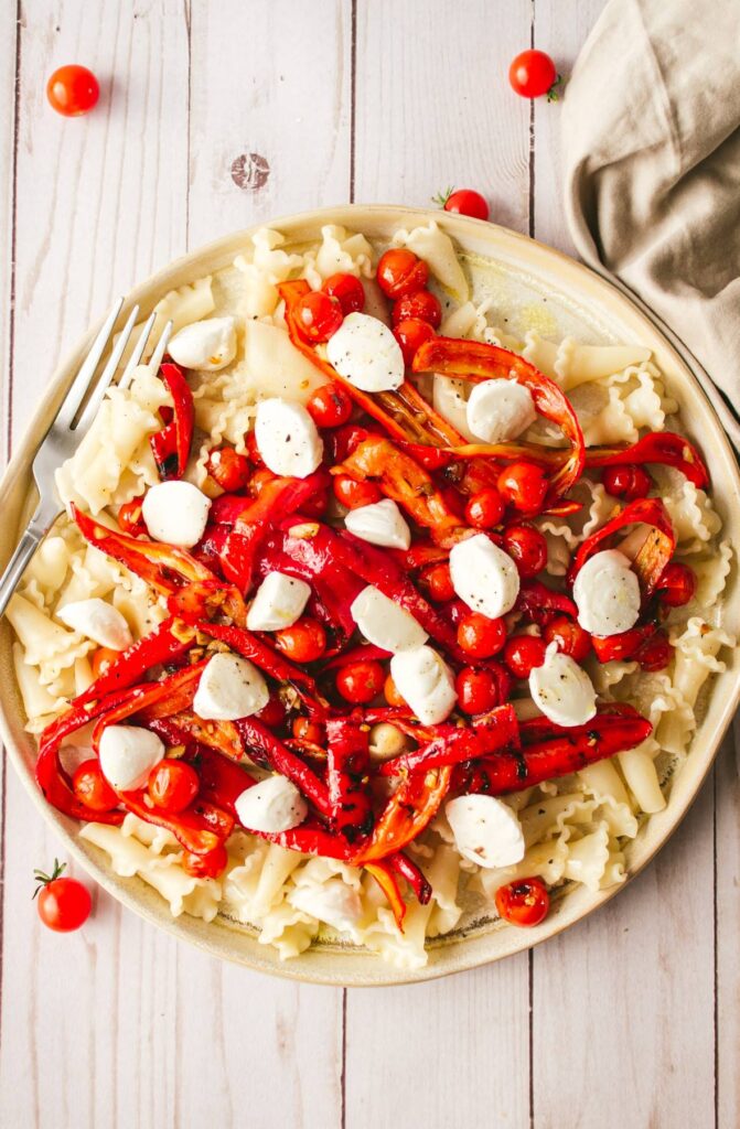 Bright image of cooked pasta with cherry tomatoes and cooked red peppers topped with small balls of fresh mozzarella