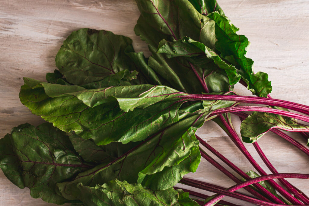 Bundle of greens and stalks from red beets scattered on a white wood table