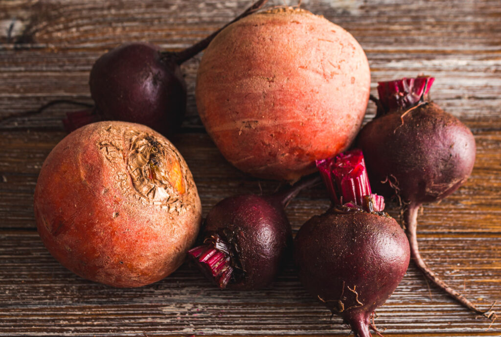 2 large golden beets and 4 small red beets on wooden background.