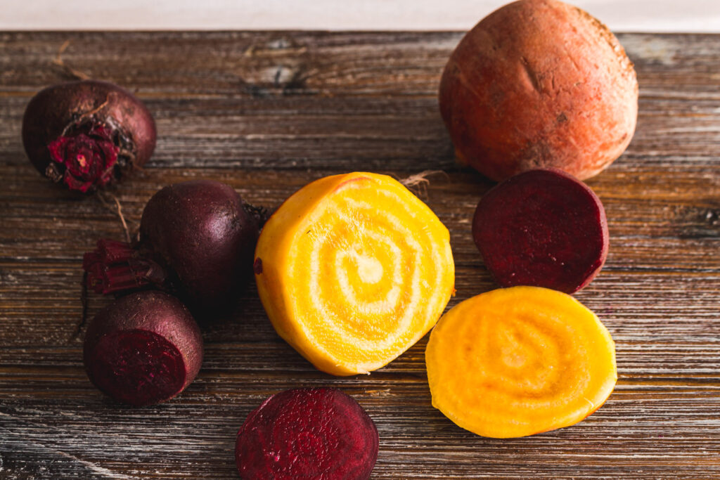 4 small red beets and 2 large golden beets. one of red beets and one of the golden beets is sliced to show the concentric rings of the root.