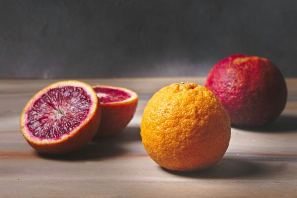Two whole blood oranges and 1 sliced in half on a wood back ground