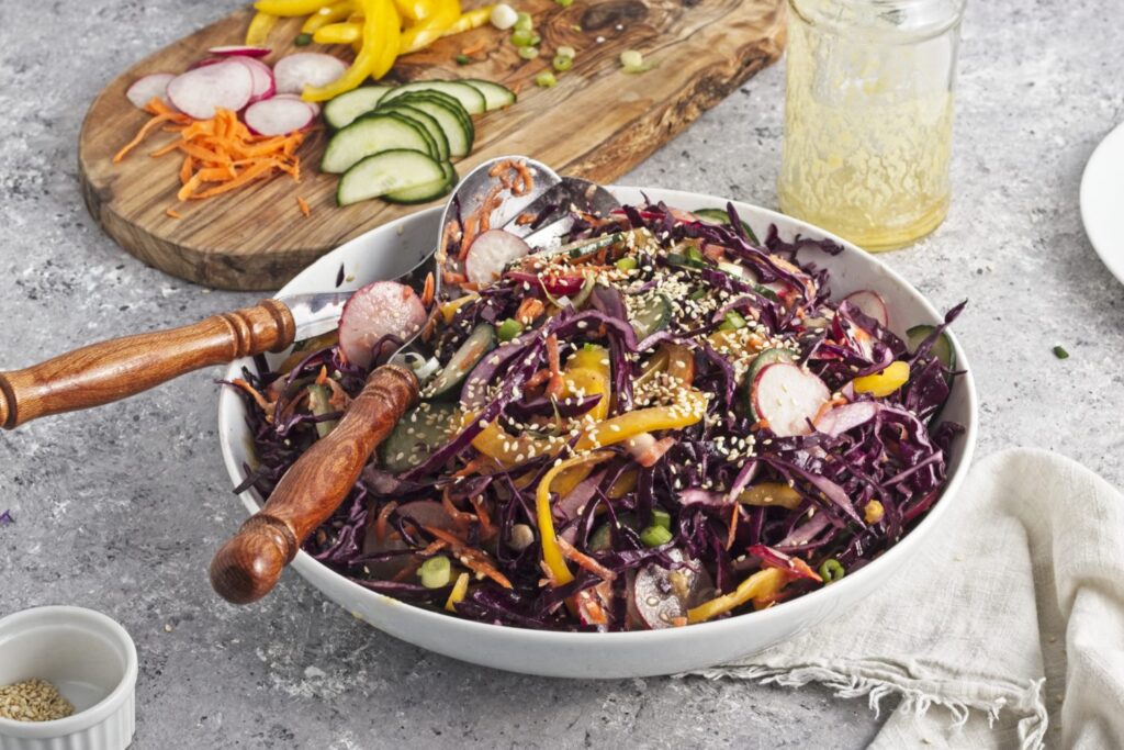 45 degree angled view of a bowl of rainbow coleslaw tossed so that the rainbow vegetables gradient is gone.