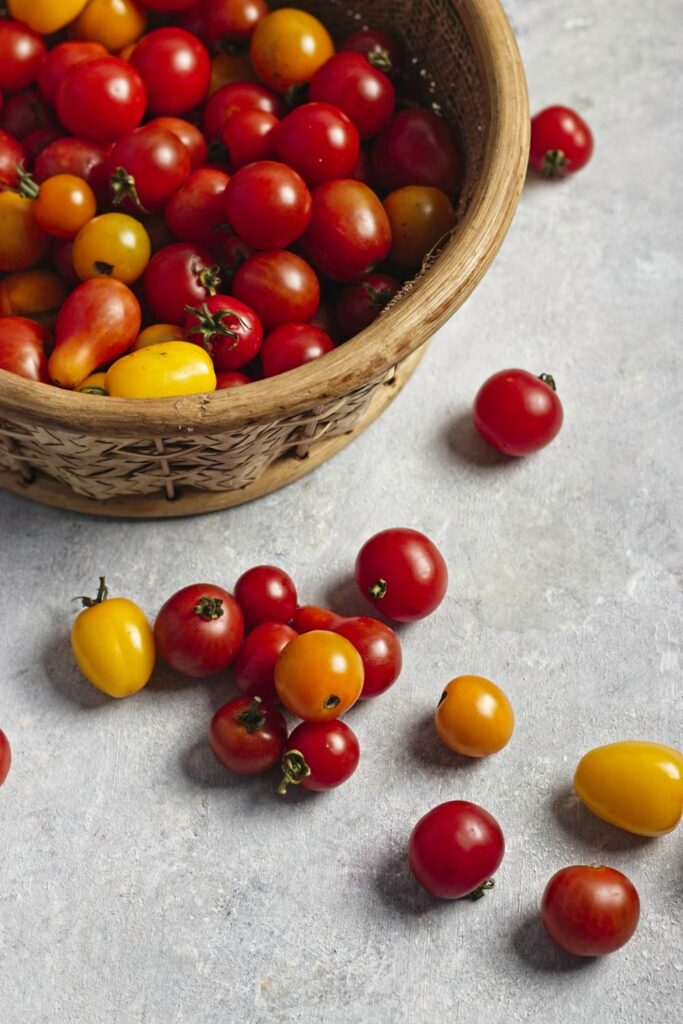 Angled view of a basket full of multicoloured cherry tomatoes with some cherry tomatoes fallen on to the grey table.