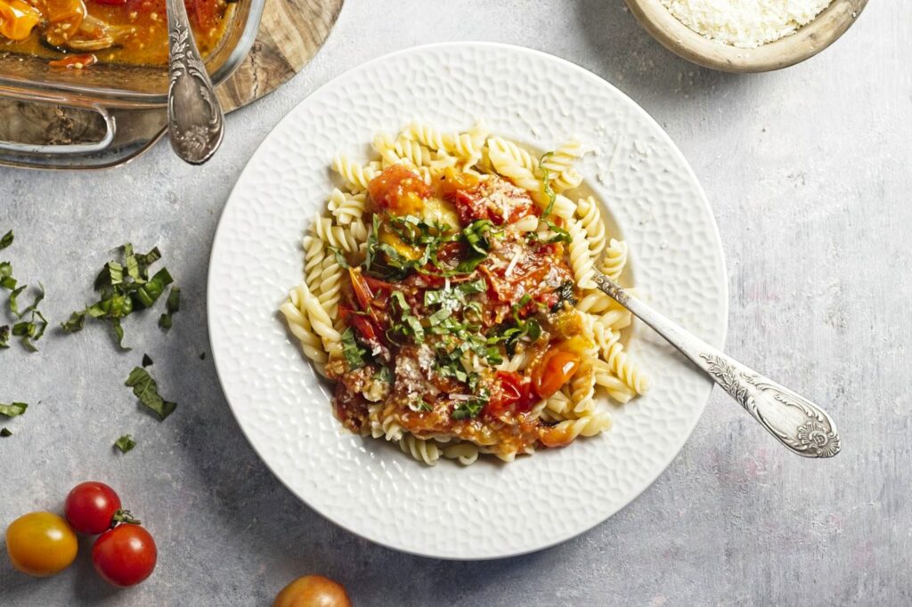 Top down view of a white dish with a heap of short pasta covered in cherry tomato sauce with a fork sticking out.